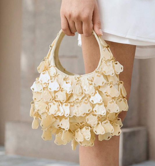 Hand holding a delicate yellow handbag with floral details against a neutral background