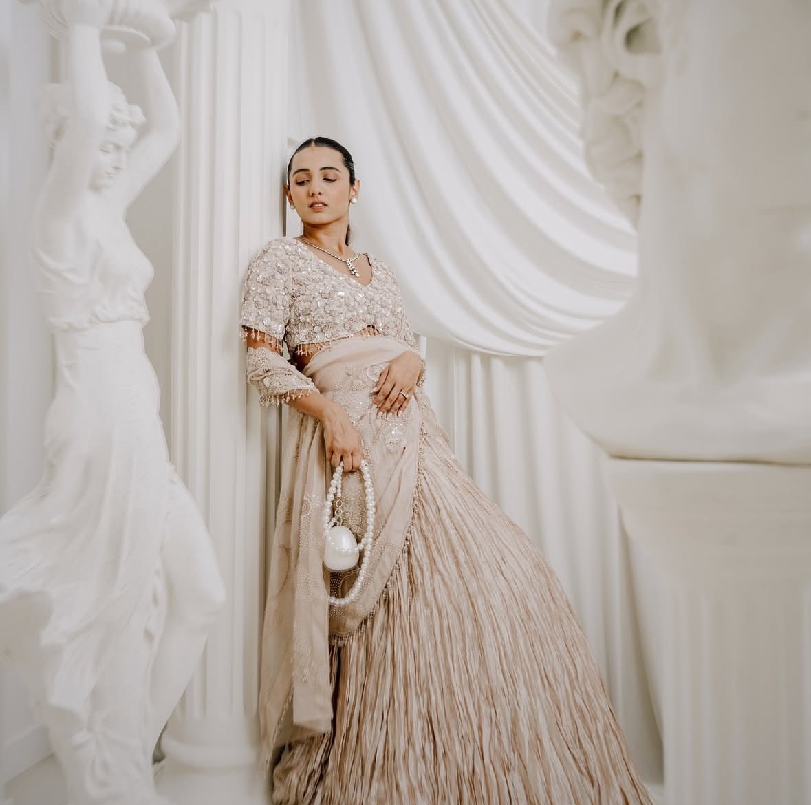 Woman in a elegant dress standing against a white curtain with pearl bag